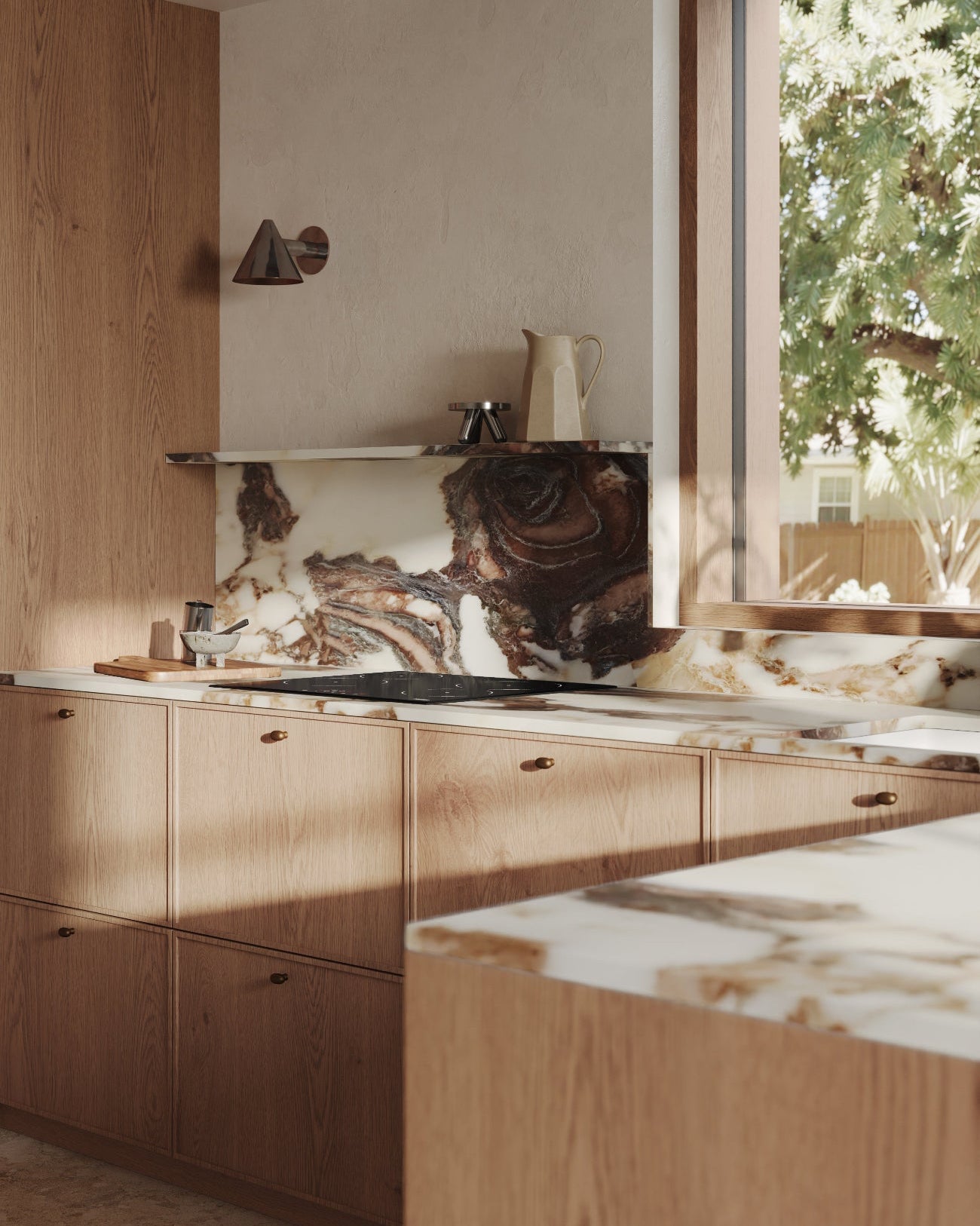 A modern kitchen interior with light oak wood cabinetry, a white and brown marble countertop and backsplash, and a large window showing greenery outside.